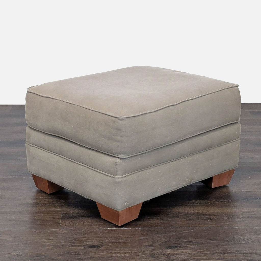 1. Square gray ottoman with plush cushion and wooden legs on a dark wood floor, angled side view.