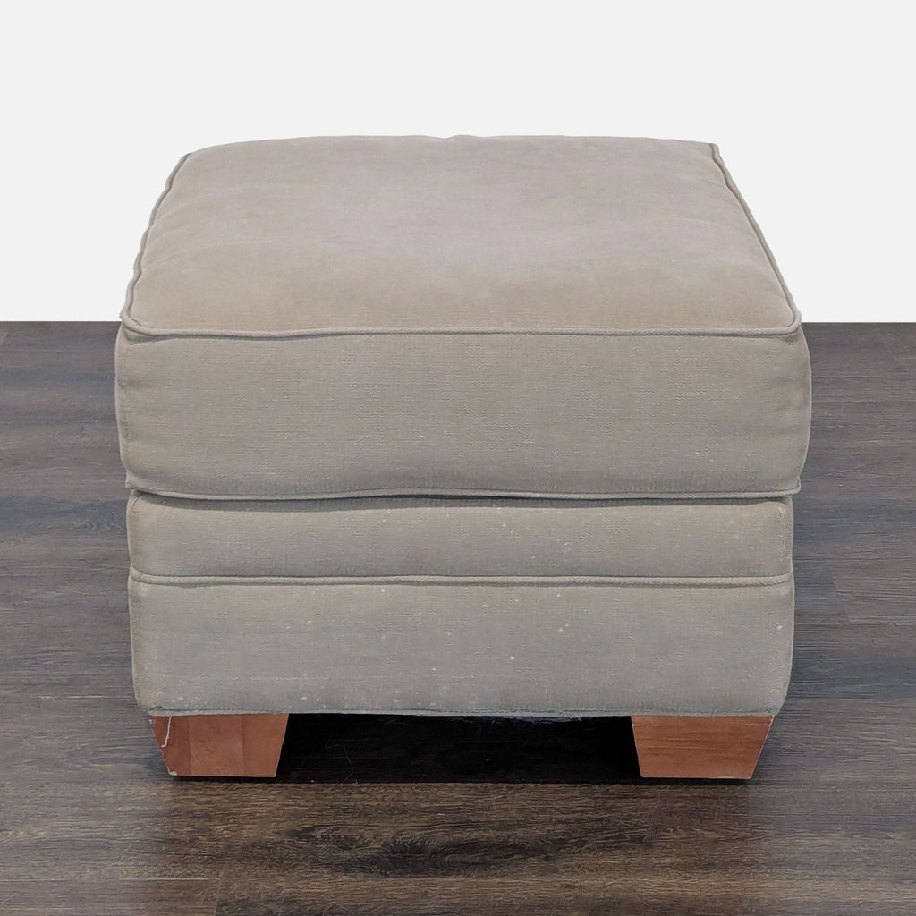 3. Overhead front view of square gray ottoman featuring soft upholstery and four wooden legs.
