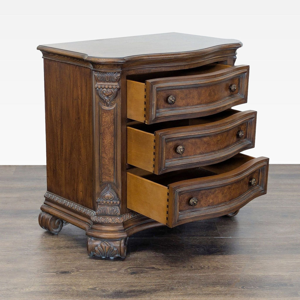 Serpentine walnut nightstand with burl details, ornate carvings, three drawers, and scrolled feet at the corners.  