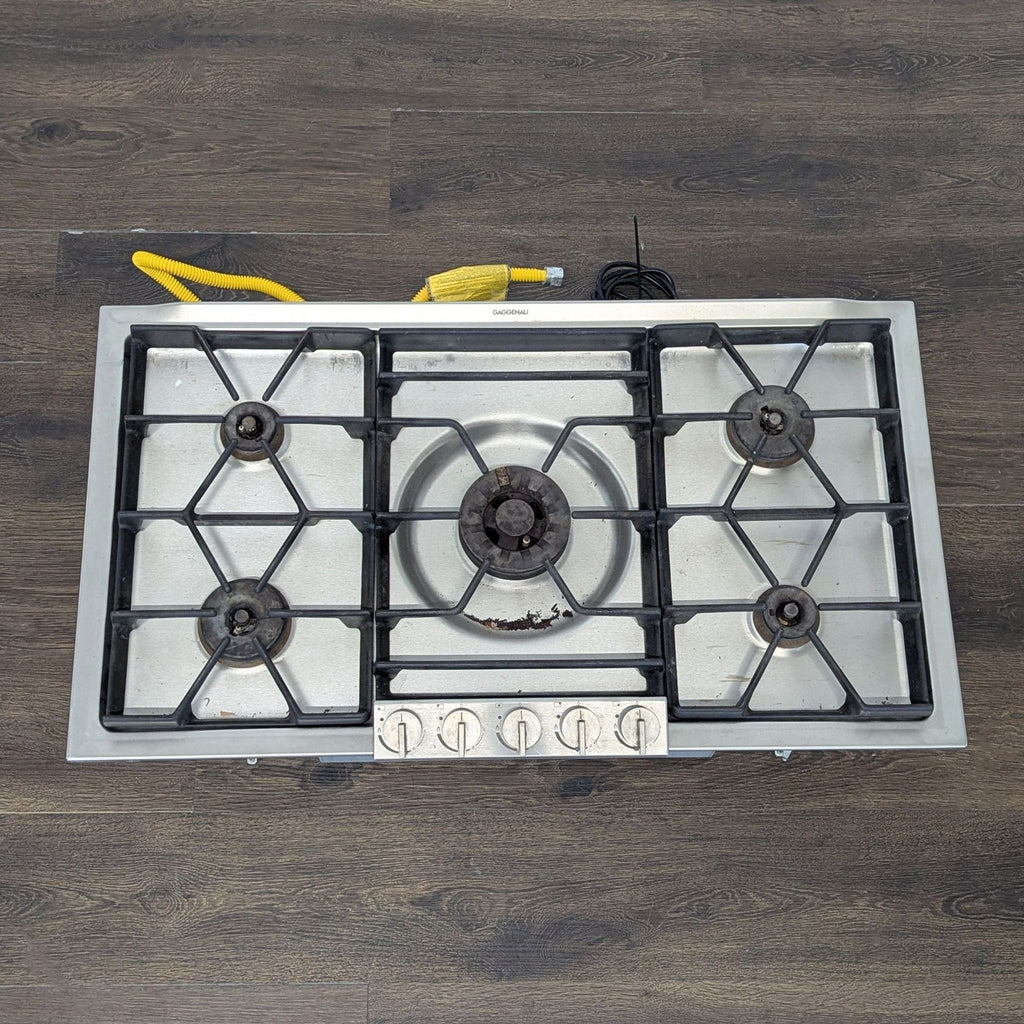 Five-burner Gaggenau gas cooktop in stainless steel, includes durable knobs and sturdy cast iron supports.