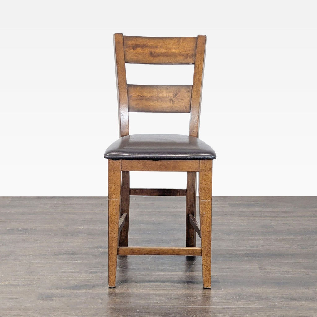 Wooden stool with ladder-back design and dark cushioned seat, viewed from the front on a wood floor.  
