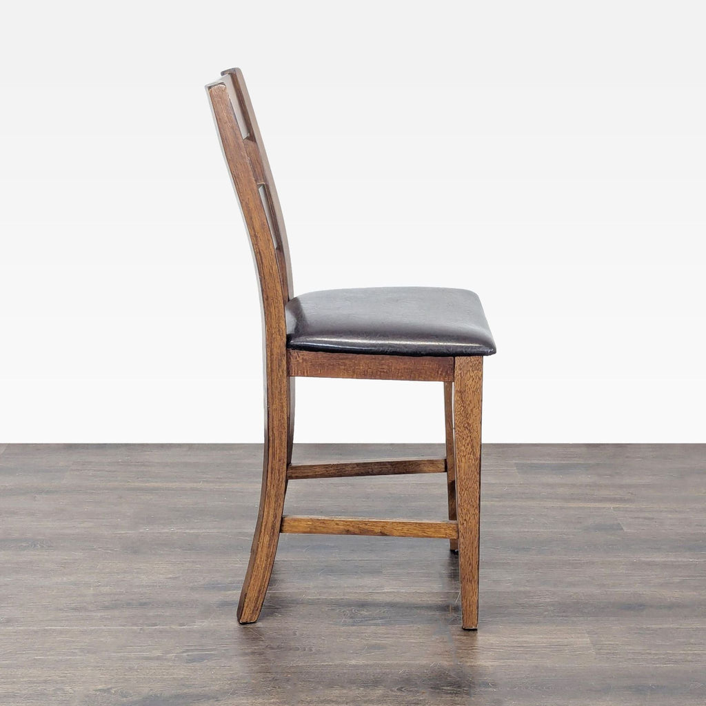 Side profile of a wooden stool with a curved ladder-back and dark padded seat, standing on hardwood flooring.  