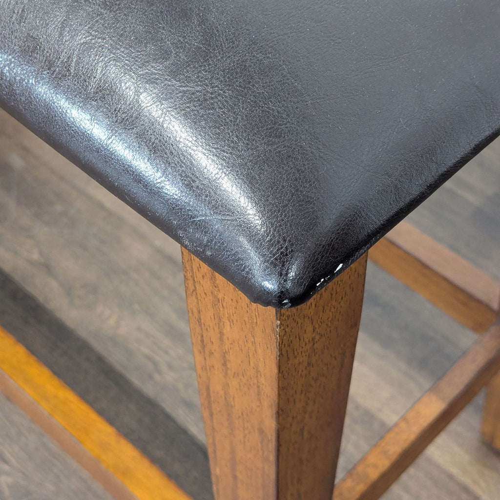 3. Close-up of the corner of a black upholstered bench seat with a wooden frame and legs.