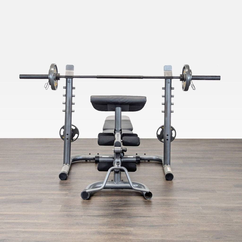Gold's Gym weight bench with barbell and plates, featuring padded supports for home strength training.
