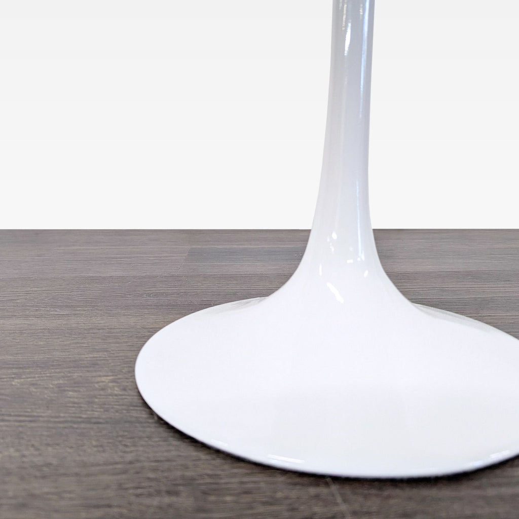 2. Close-up of the glossy white pedestal base of a contemporary end table on dark wood flooring.