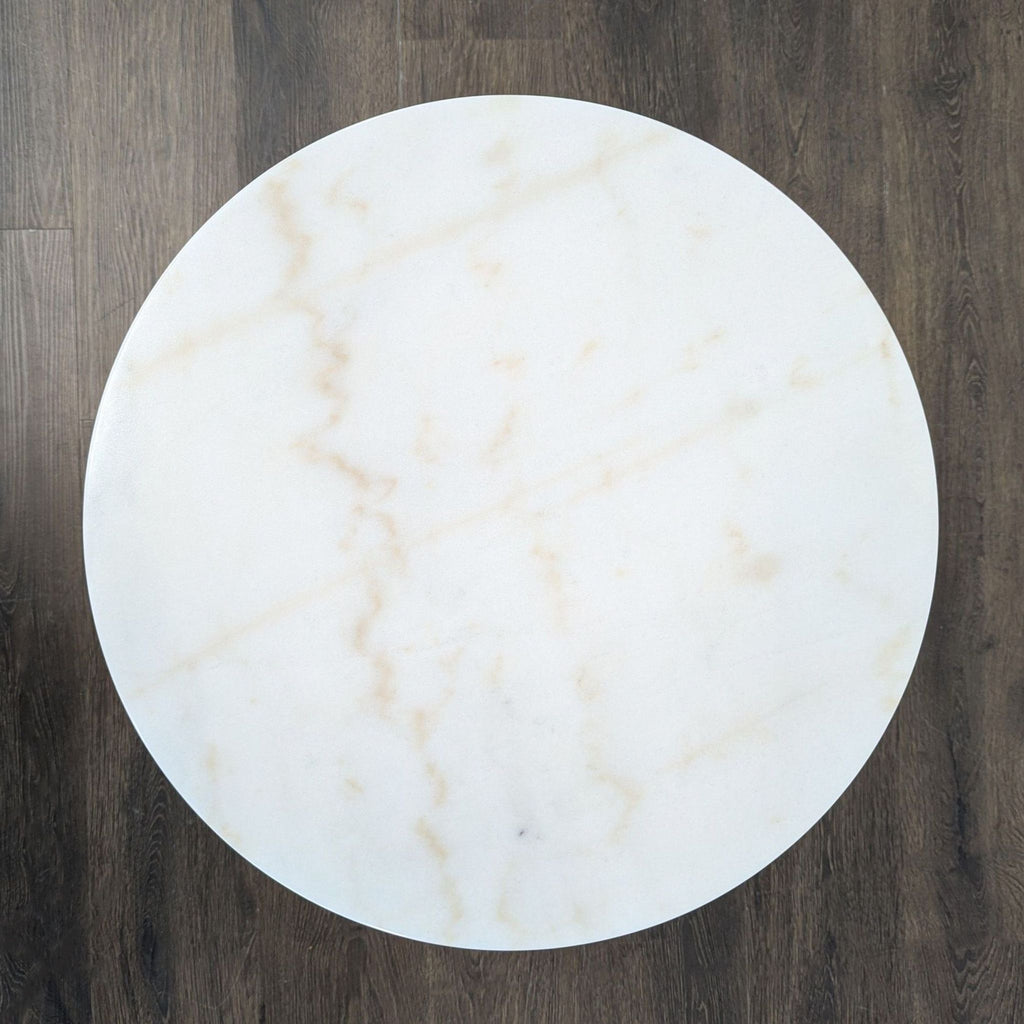 3. Overhead view of a round white marble end table top with subtle veining on a wood floor background.