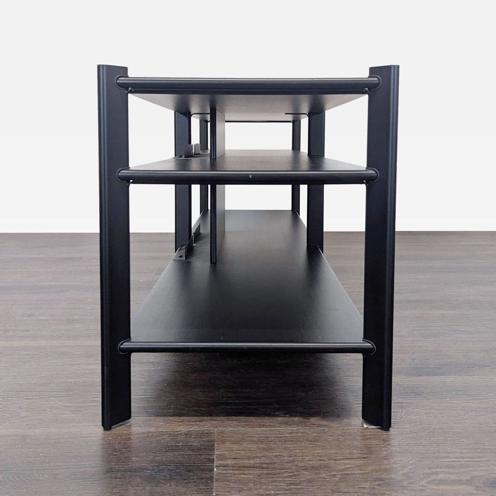 Front view of an Ikea black three-shelf unit with metal supports, positioned on a dark wood floor.