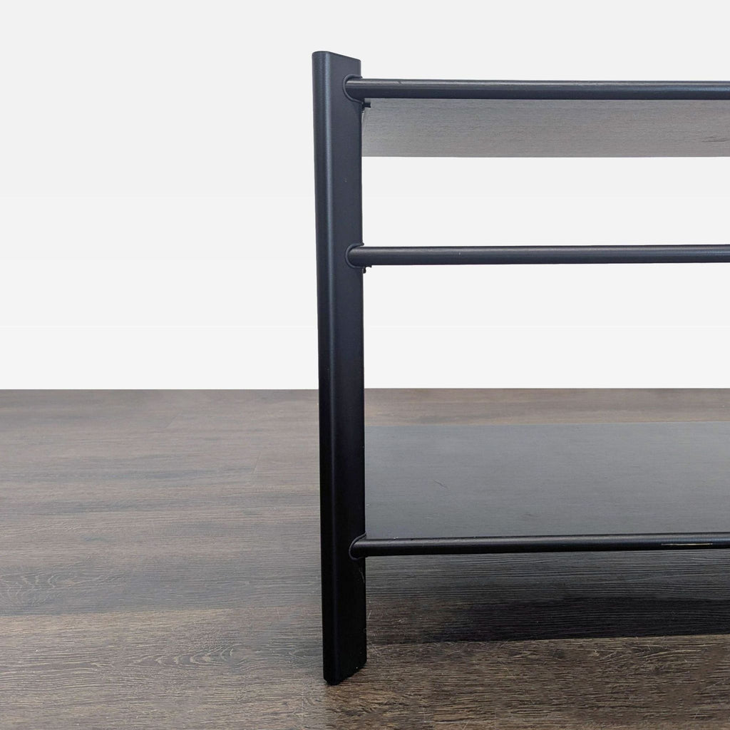 Side view of an Ikea three-tier black shelving unit with metal frame on a wood floor.  