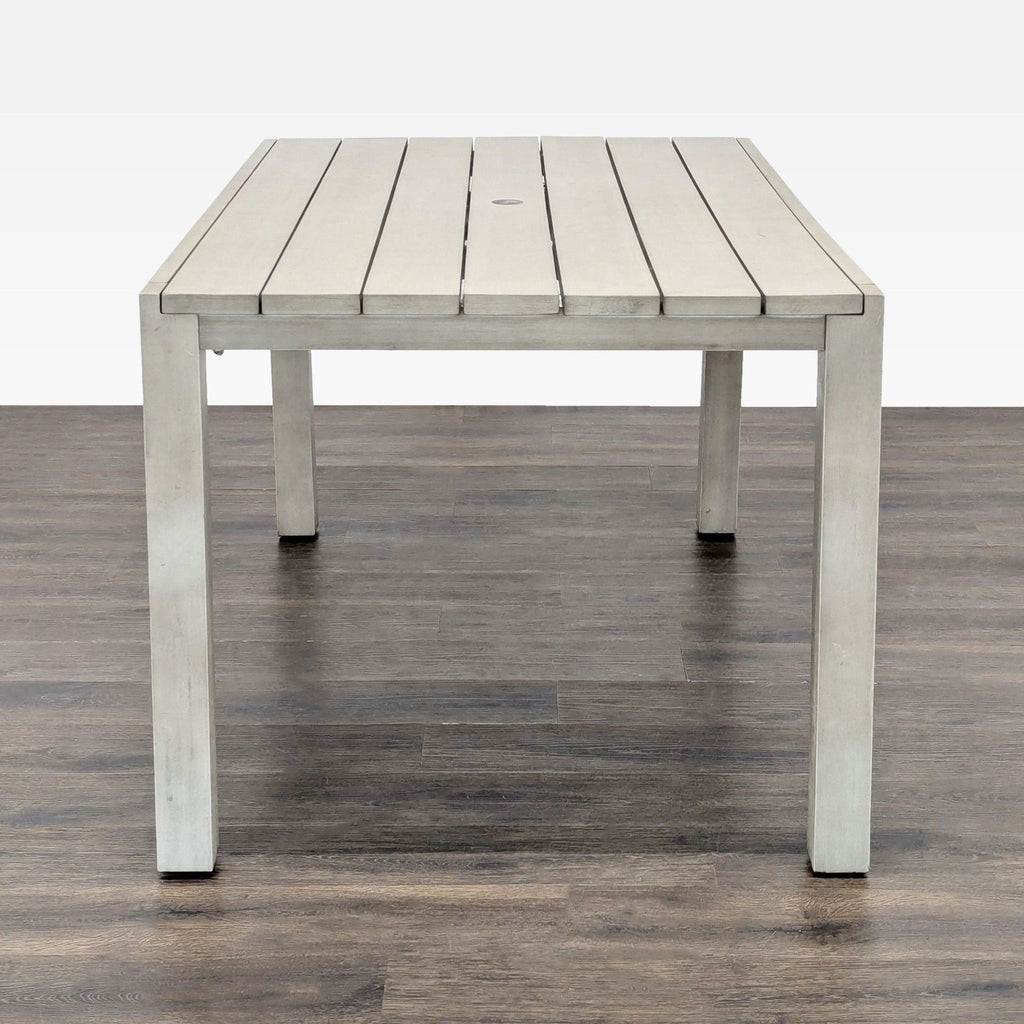 Rectangular light grey CB2 table with clean lines and a slatted surface, featuring a center umbrella hole.