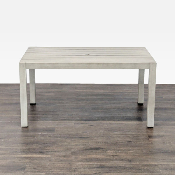 Modern CB2 dining table with slatted light grey top, sturdy legs, and center hole, shown on wood floor.