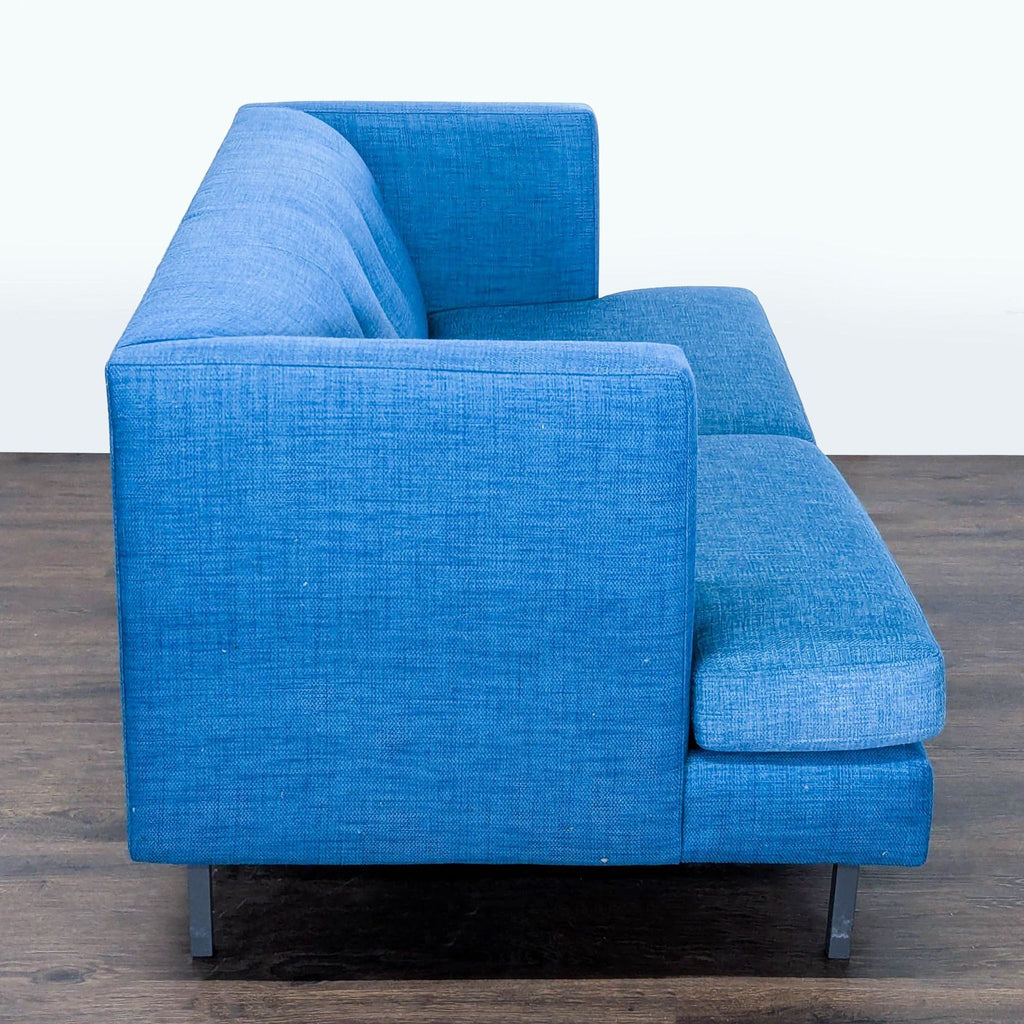 3. End view of a CB2 blue loveseat with boxy shape and tufted upholstery, perfect for apartments.