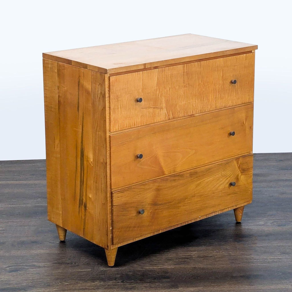 3. Angled view of a sturdy, natural-finish dresser featuring three drawers and minimalist metal hardware.