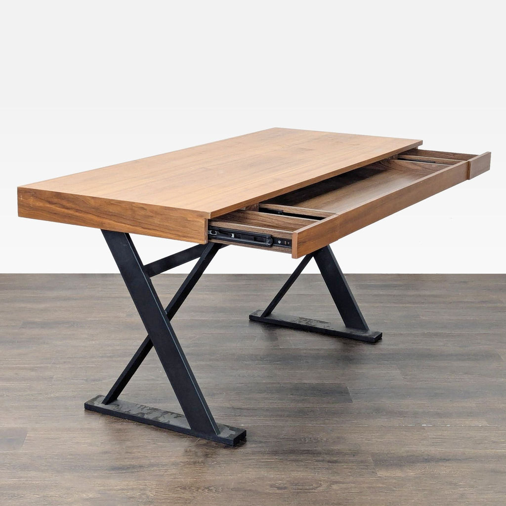 2. Angled view of Moe's desk with a spacious wooden top, black metal X-legs, and an open sliding storage drawer.