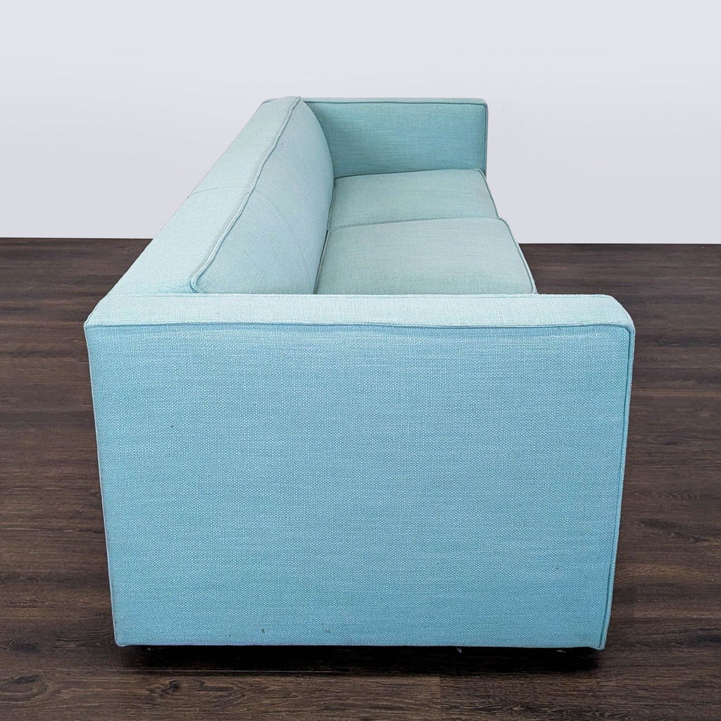 3. Side perspective of a modern CB2 3-seat sofa in light blue fabric, displaying straight arm and back design.
