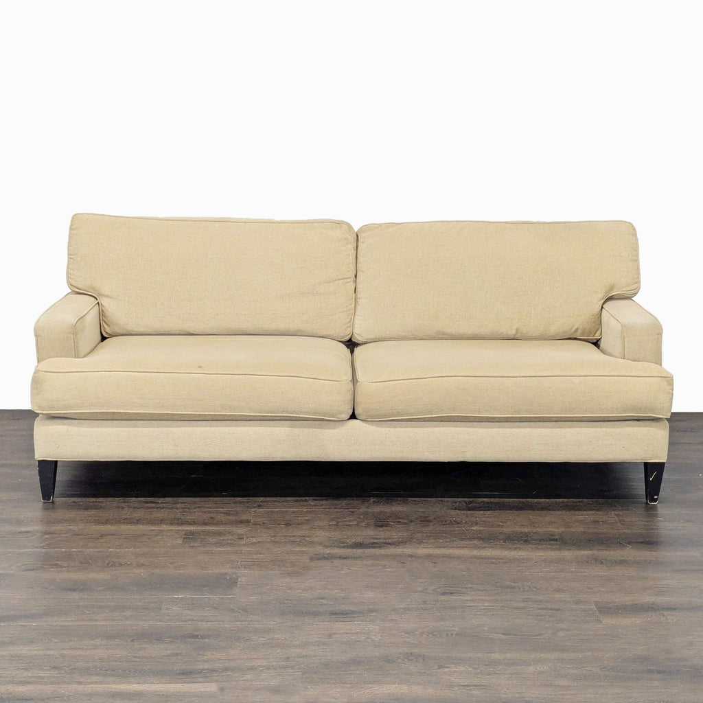 A beige Pier 1 Imports 3-seat sofa with plush cushions and dark legs, shown on a wood floor.  