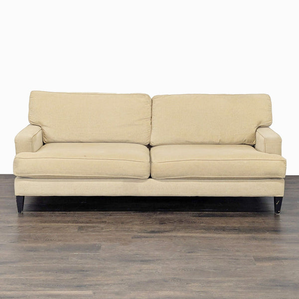 A beige Pier 1 Imports 3-seat sofa with plush cushions and dark legs, shown on a wood floor.  