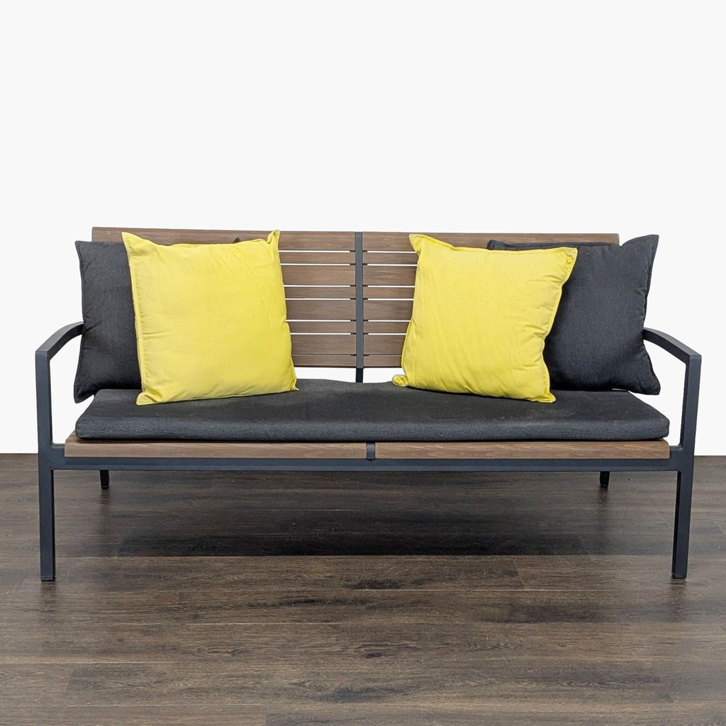 Crate & Barrel bench with black metal frame, wooden slats, grey seat, and yellow/grey cushions, seats three.