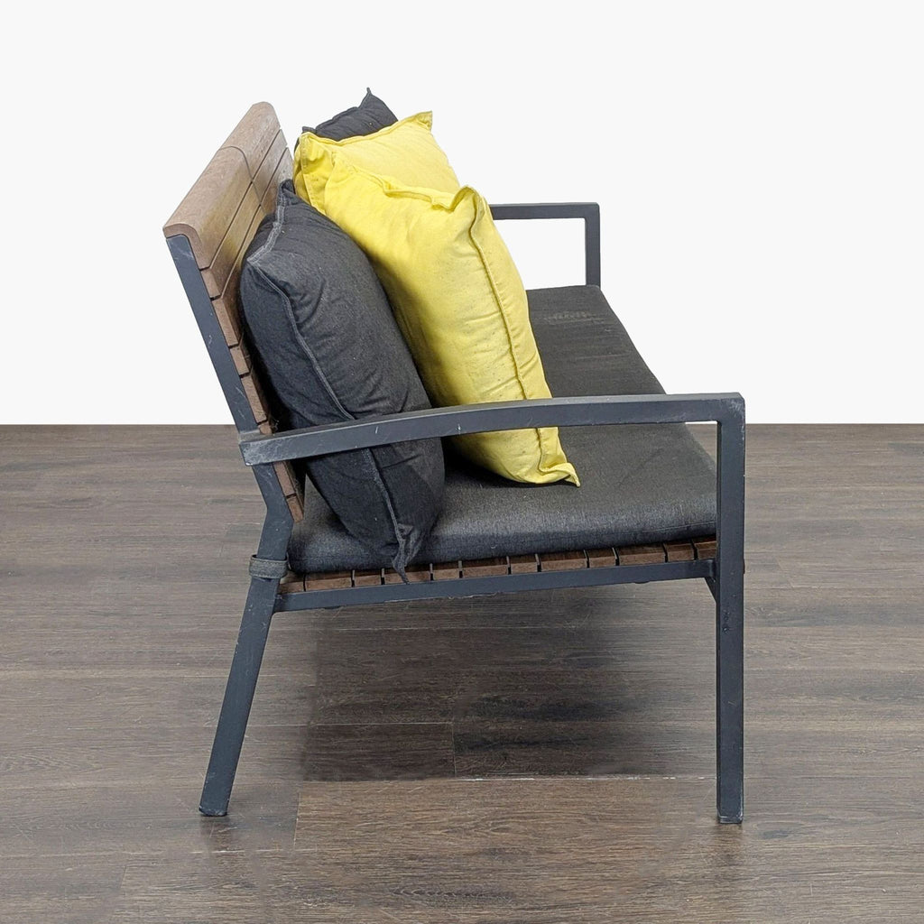 Side view of a Crate & Barrel bench featuring a sleek black frame, wood slats, and plush yellow and grey pillows.