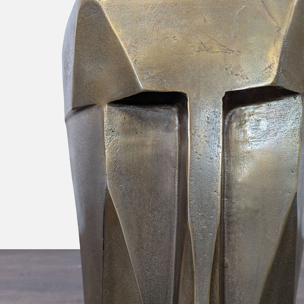 Close-up view of the metallic bronze geometric face on a sculptural accent stool, highlighting sharp details.