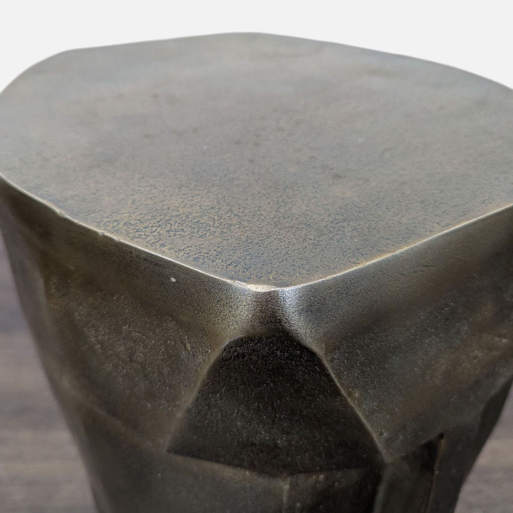Angled top view of a compact, metallic bronze sculptural stool featuring a modern, geometric finish.