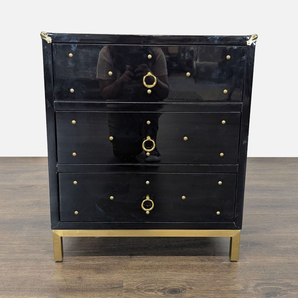 1. Black Chic Home dresser with three drawers, gold ring pulls, gold studs, and gold metal legs on wood floor.  