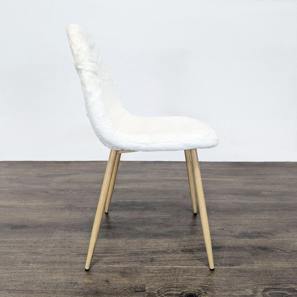 Side view of a dining chair featuring white fake fur upholstery and angled wooden legs, on dark wood flooring.  