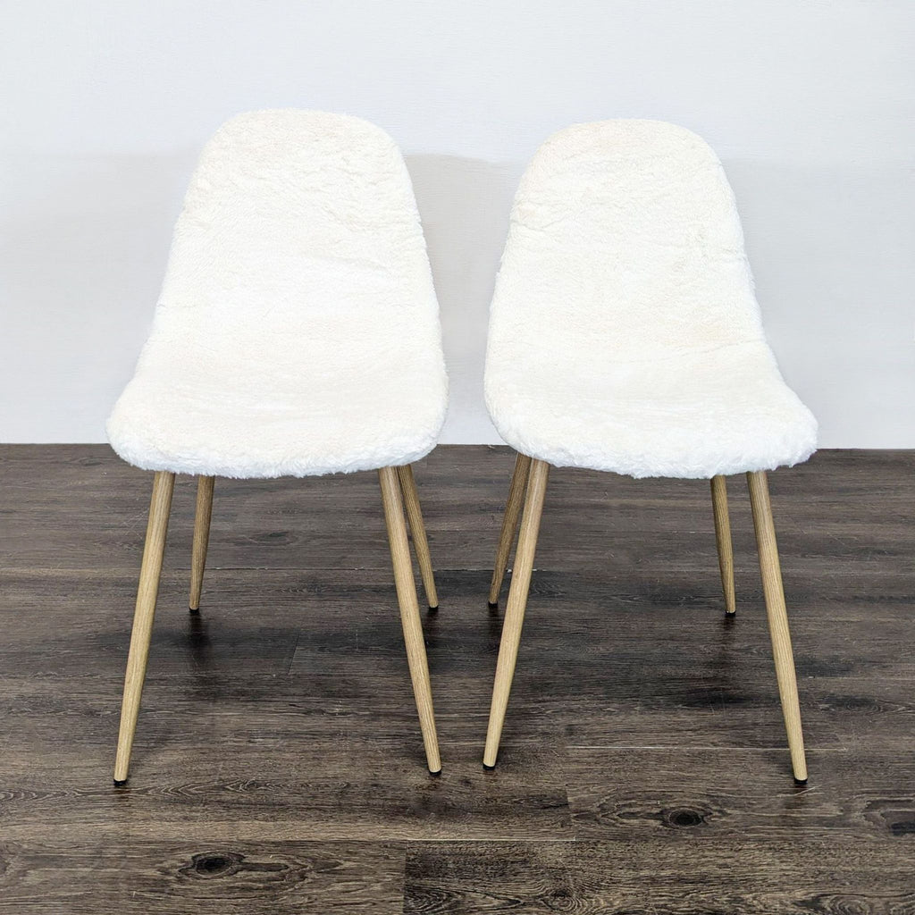 Two dining chairs with white fake fur upholstery and wooden legs, placed on a dark wood floor.  