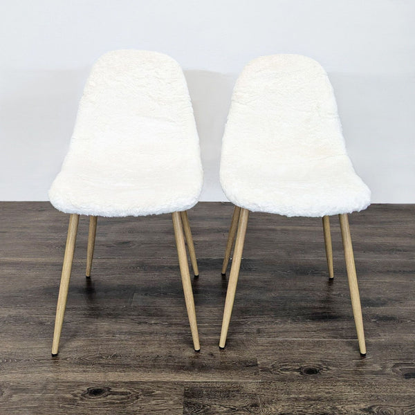 Two dining chairs with white fake fur upholstery and wooden legs, placed on a dark wood floor.  