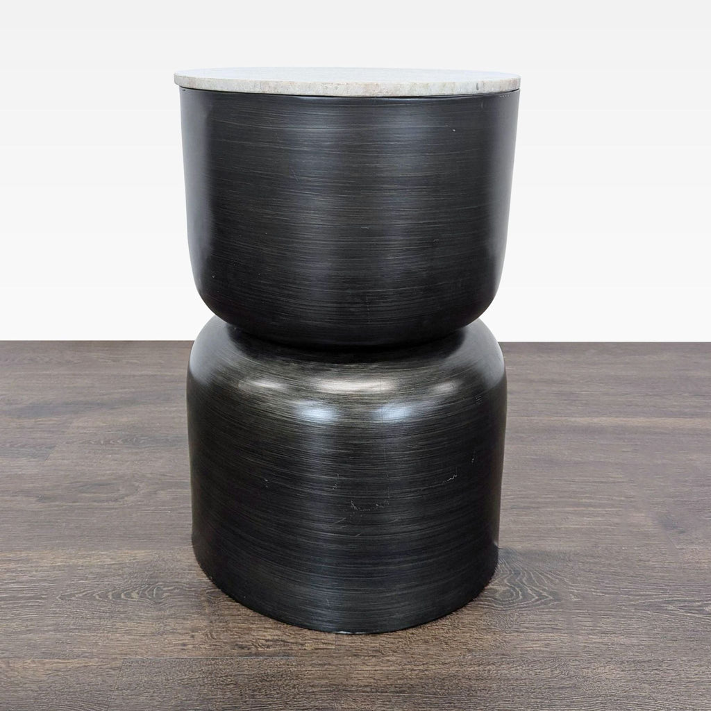 1. Modern side table with a sculptural black metal base and round, light stone top on wooden flooring.