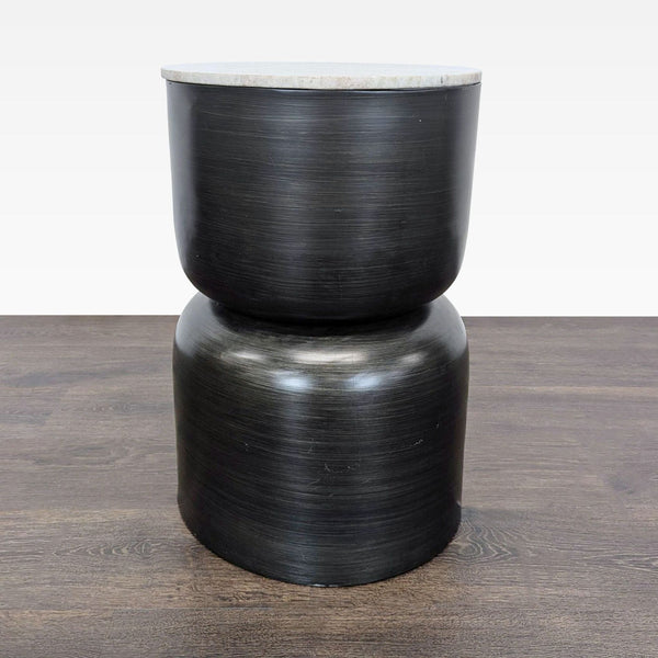 1. Modern side table with a sculptural black metal base and round, light stone top on wooden flooring.