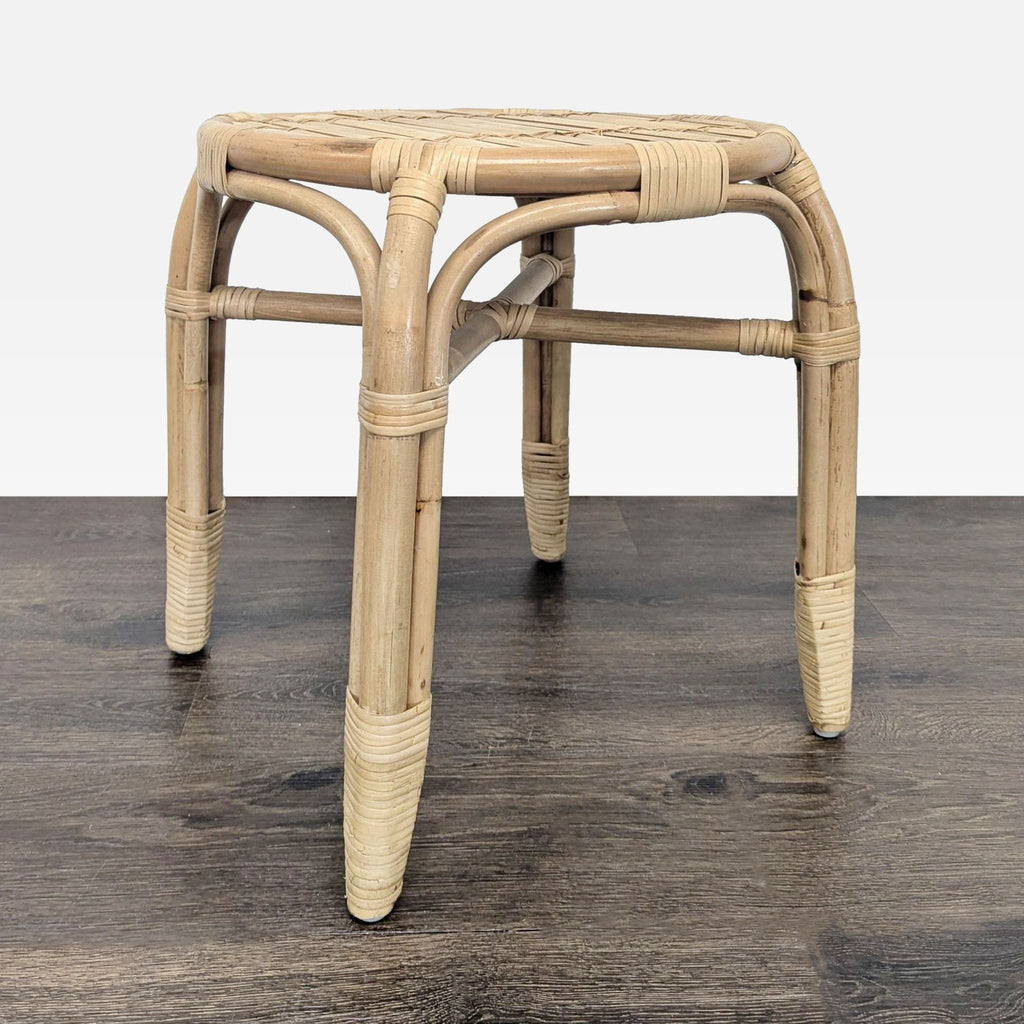 Close-up angled view of a natural rattan stool with bamboo accents on its legs and seat, on wood floor.