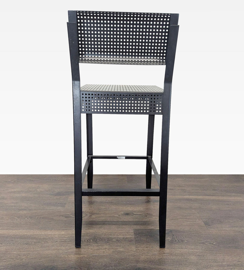 3. Rear view of an Ikea bar stool, black metal with perforated seat and backrest, on dark wooden flooring.
