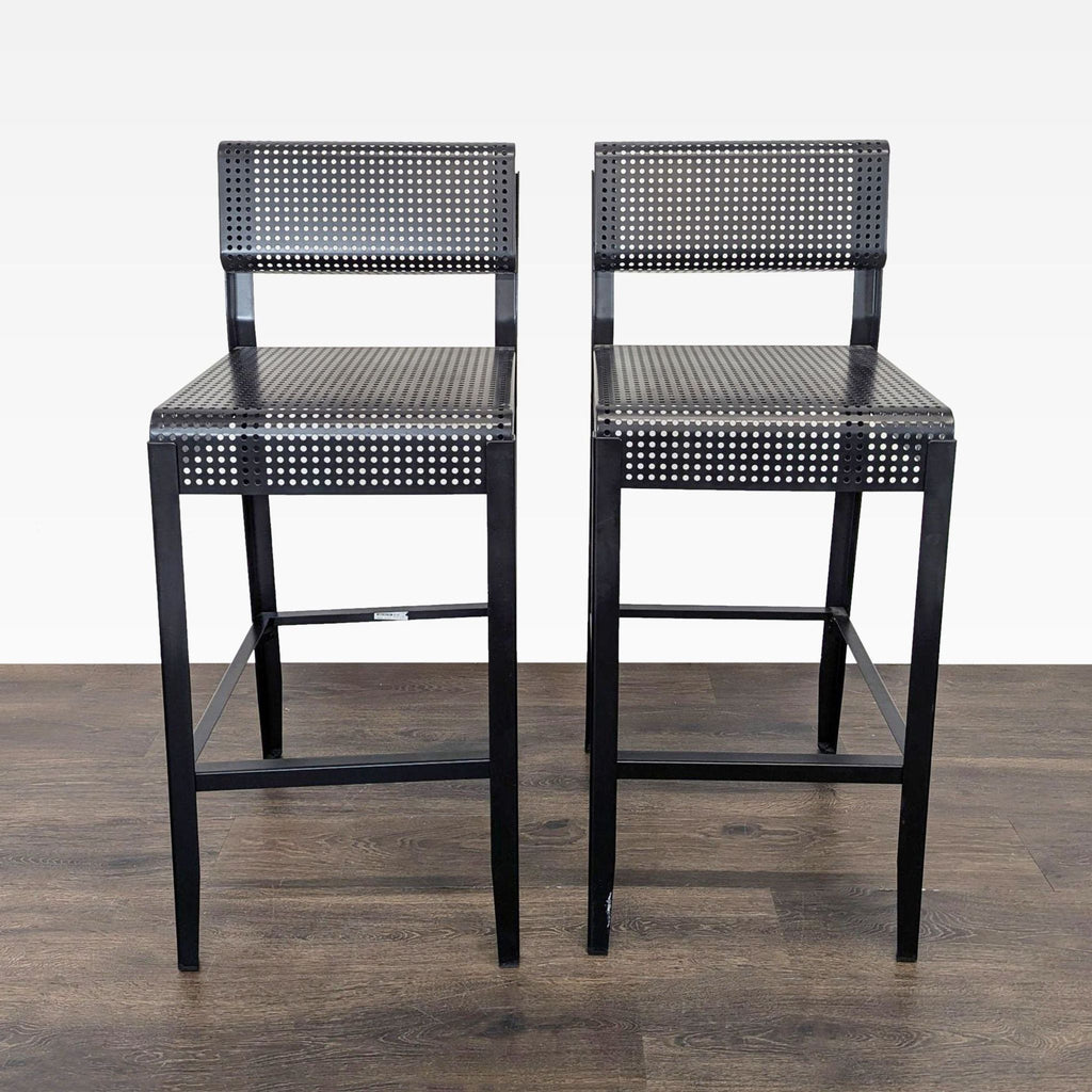 1. Pair of black metal Ikea bar stools with perforated seat and backrest on wooden floor, front view.