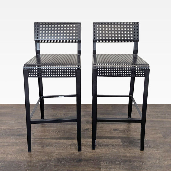 1. Pair of black metal Ikea bar stools with perforated seat and backrest on wooden floor, front view.