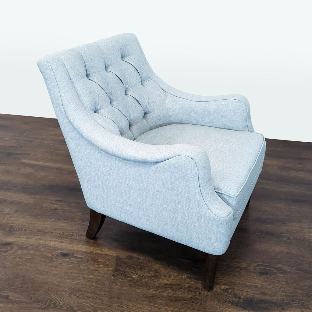 Elegant lounge chair in soft blue fabric, tufted detailing, cushioned seat, and sturdy dark wood legs.