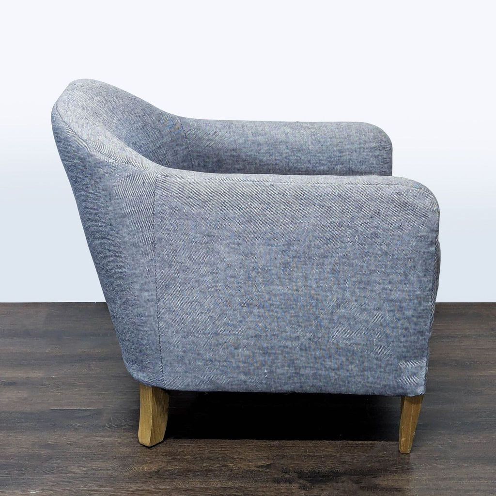 Modern Restoration Hardware lounge chair with soft blue fabric, curved backrest, and wooden legs for comfort.