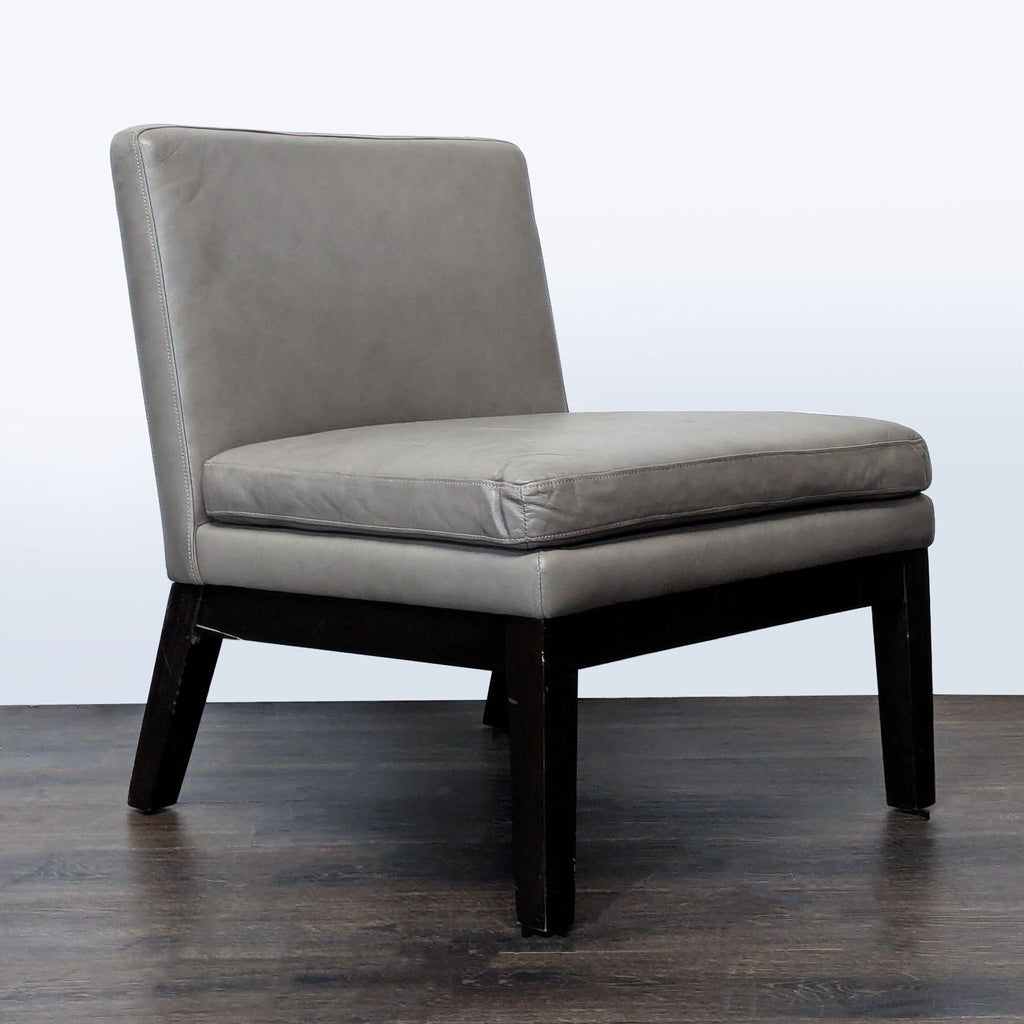 2. Angled view of a modern West Elm lounge chair featuring gray leather and sturdy dark wood legs.