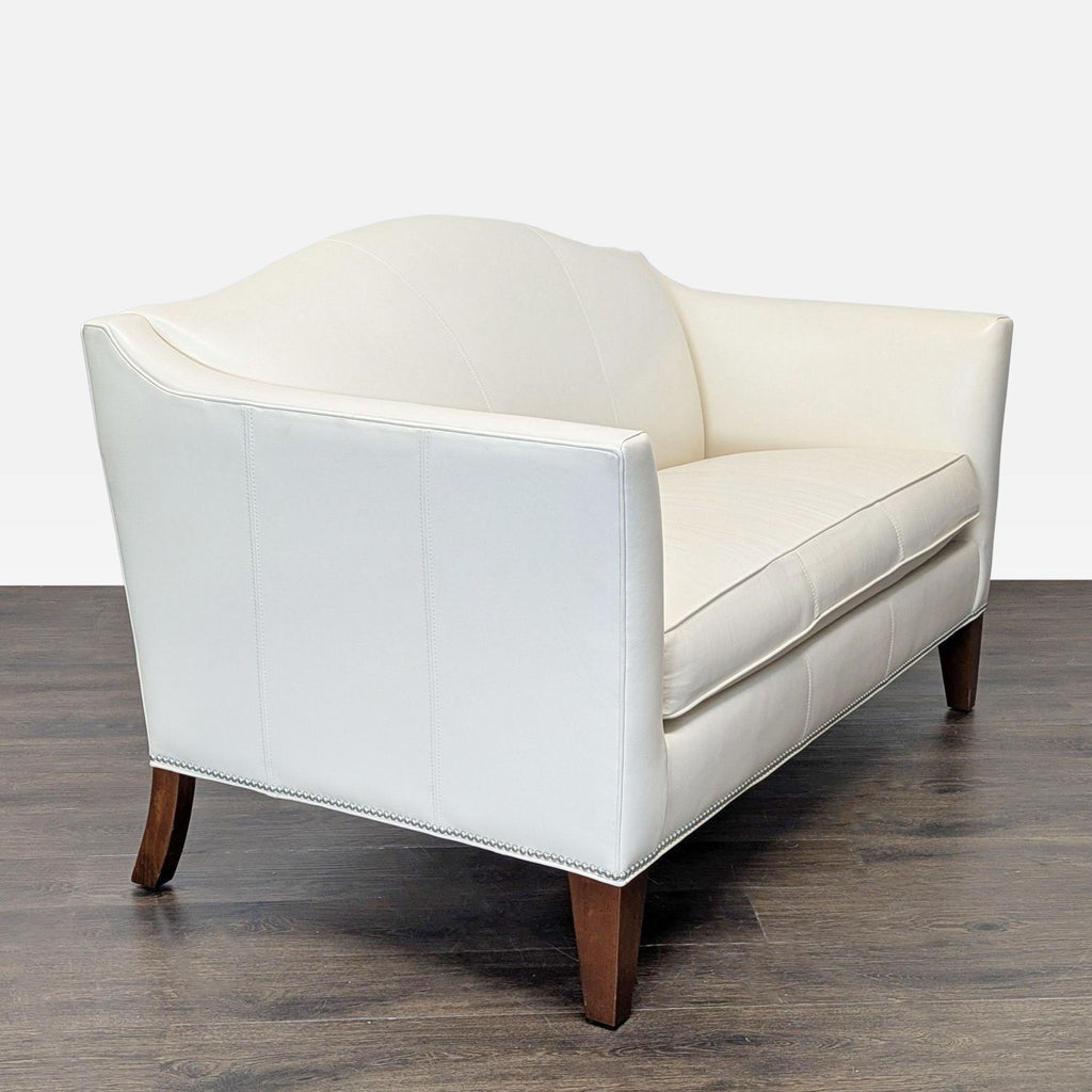 Compact cream leather loveseat by Ethan Allen, featuring clean lines, nailhead accents, and sturdy wood base.