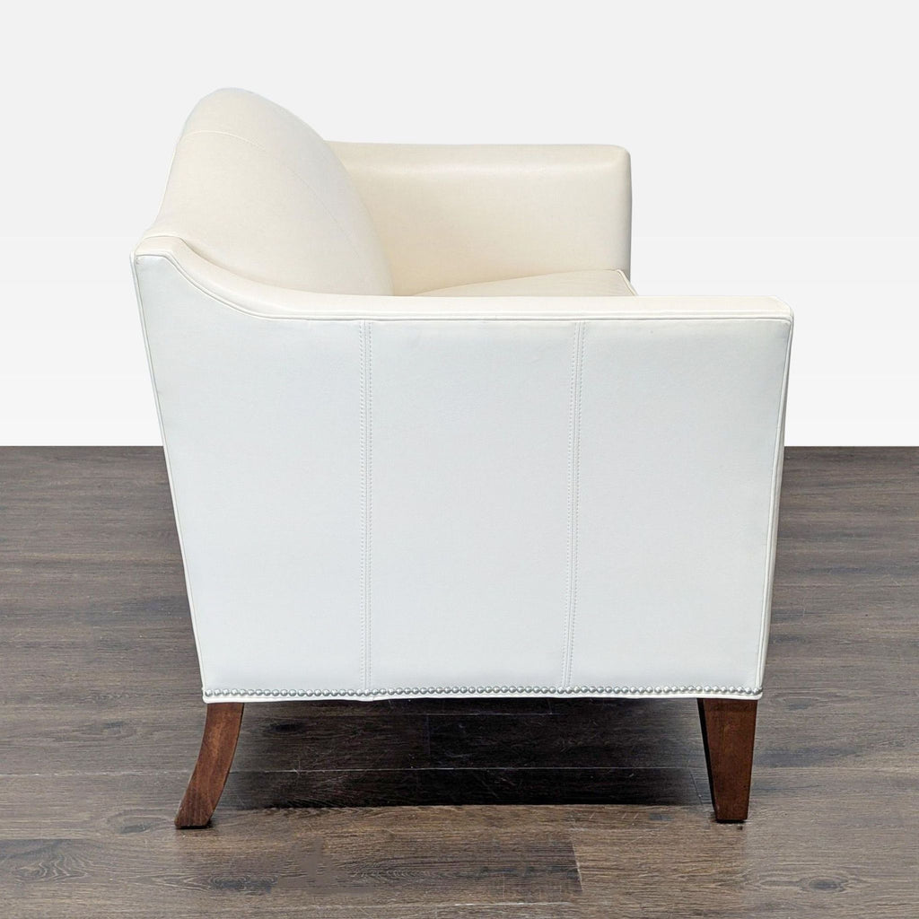 Modern Ethan Allen loveseat with smooth cream upholstery, silver trim, and wooden legs, fits any decor style.