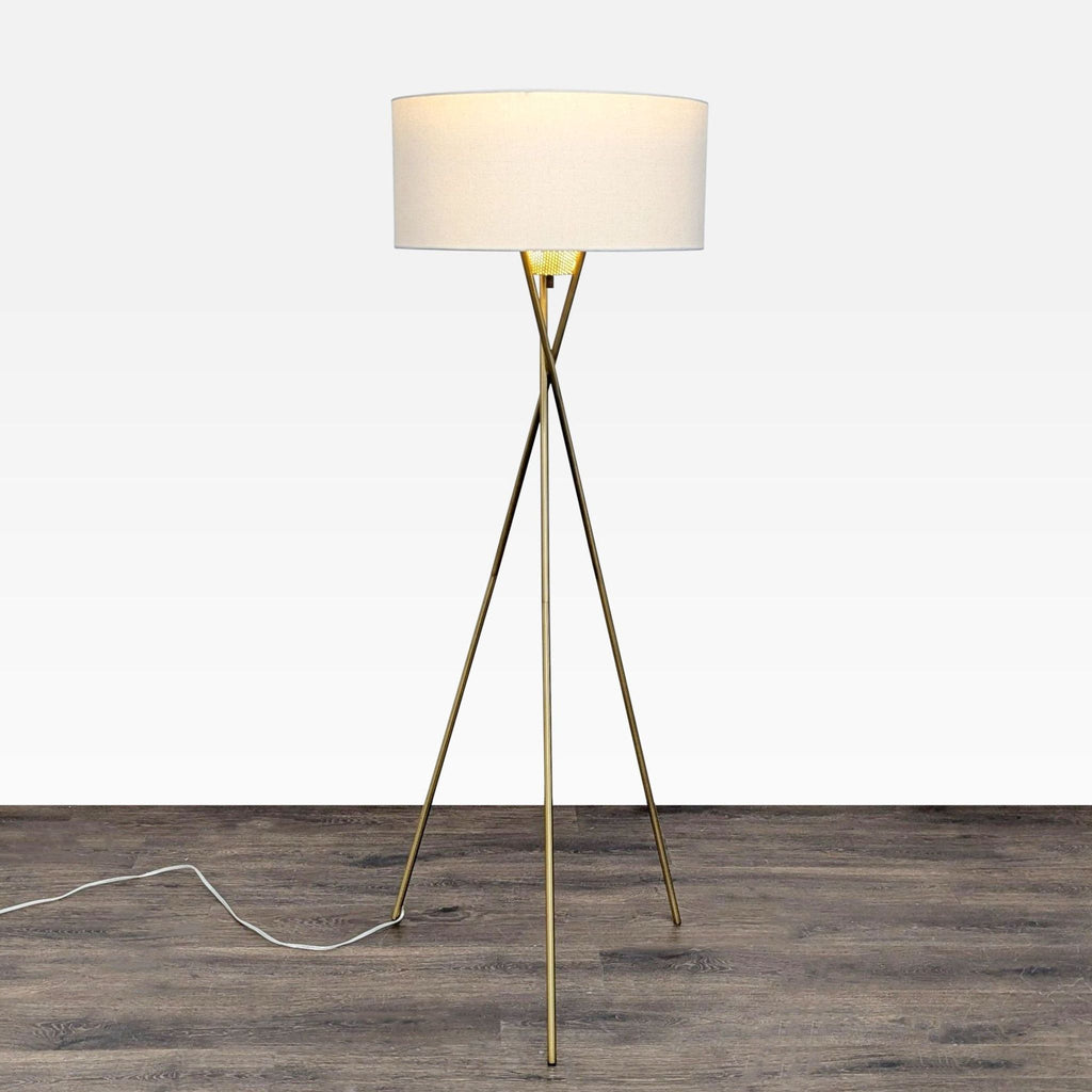 Brass tripod floor lamp with white drum shade and perforated diffuser, ideal for modern living rooms or offices.  