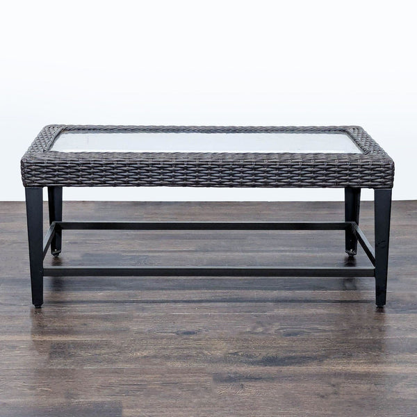 Rectangular table with metal frame, wicker border, and glass top, suitable for indoor or outdoor spaces.  