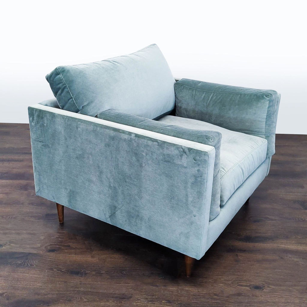 Modern lounge chair in soft blue velvet, featuring simple lines, plush comfort, and sturdy wooden legs.  