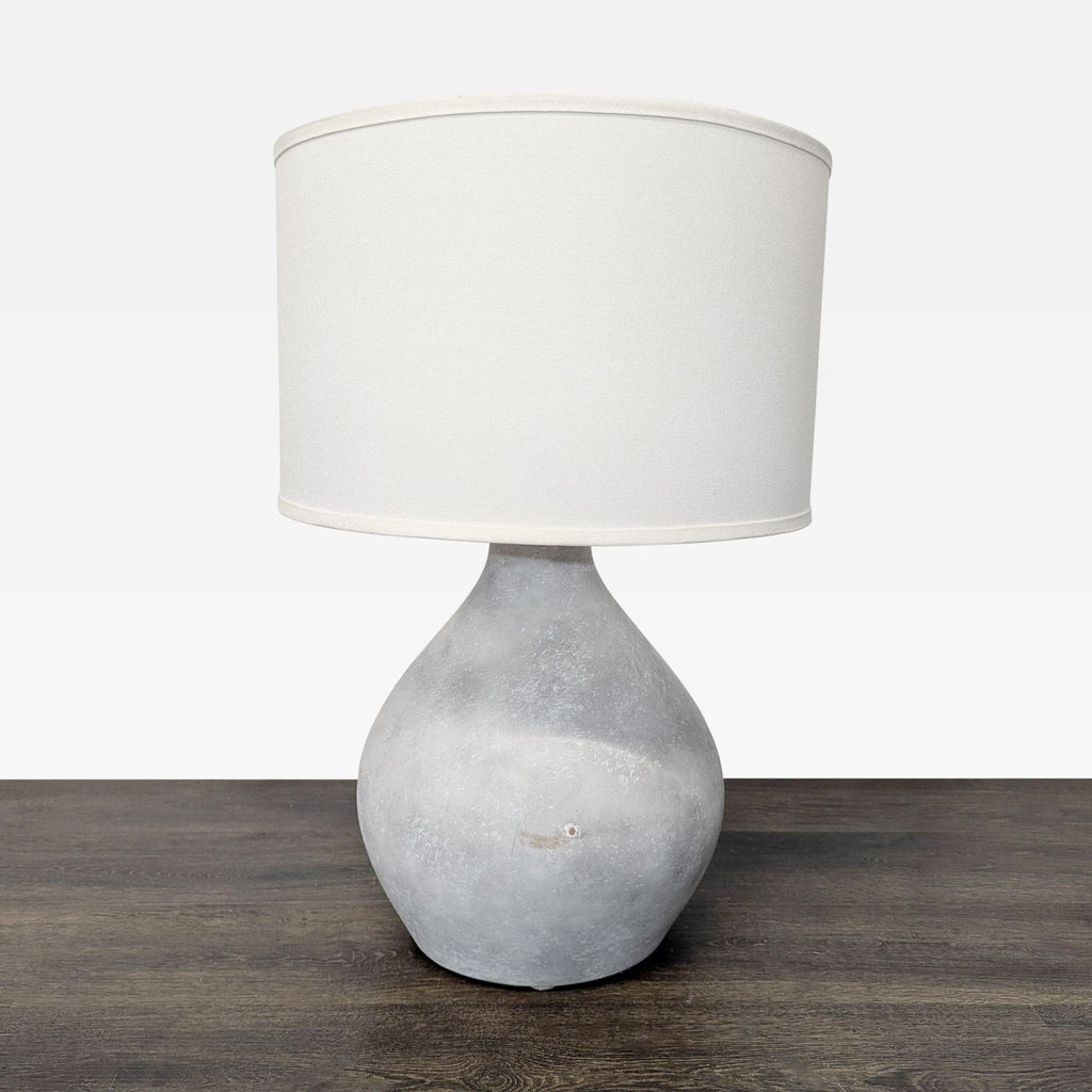 Pottery Barn table lamp with a rounded gray ceramic base and white drum shade, shown on a wooden table.