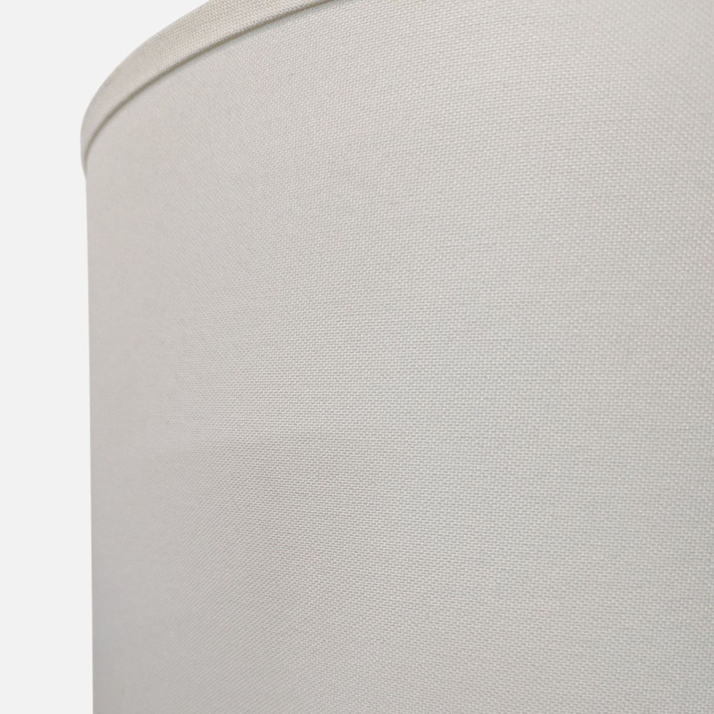 Close-up of a Pottery Barn lamp with a smooth ceramic gray base and classic white drum shade.