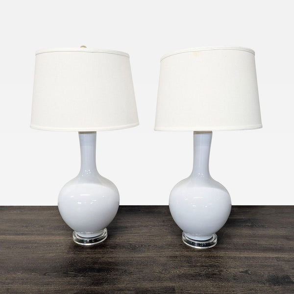 Pair of white ceramic Safavieh table lamps with fabric drum shades and clear bases, modern and elegant design.