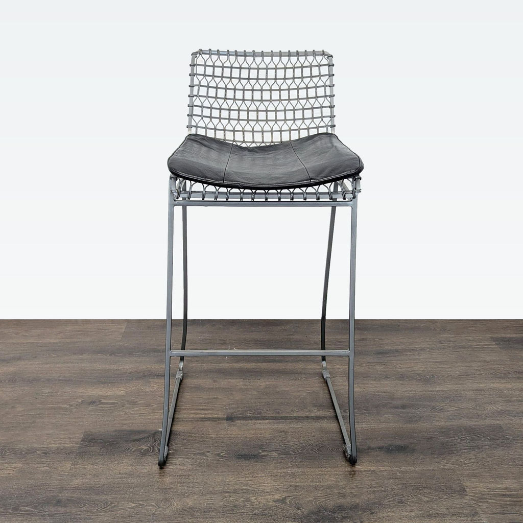 3. Front view of a Crate & Barrel iron bar stool with a geometric wire back and cushioned black seat.