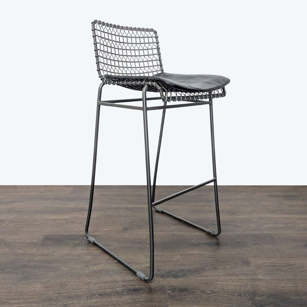 2. Side view of a modern Crate & Barrel bar stool featuring a welded wire frame and black seat cushion.