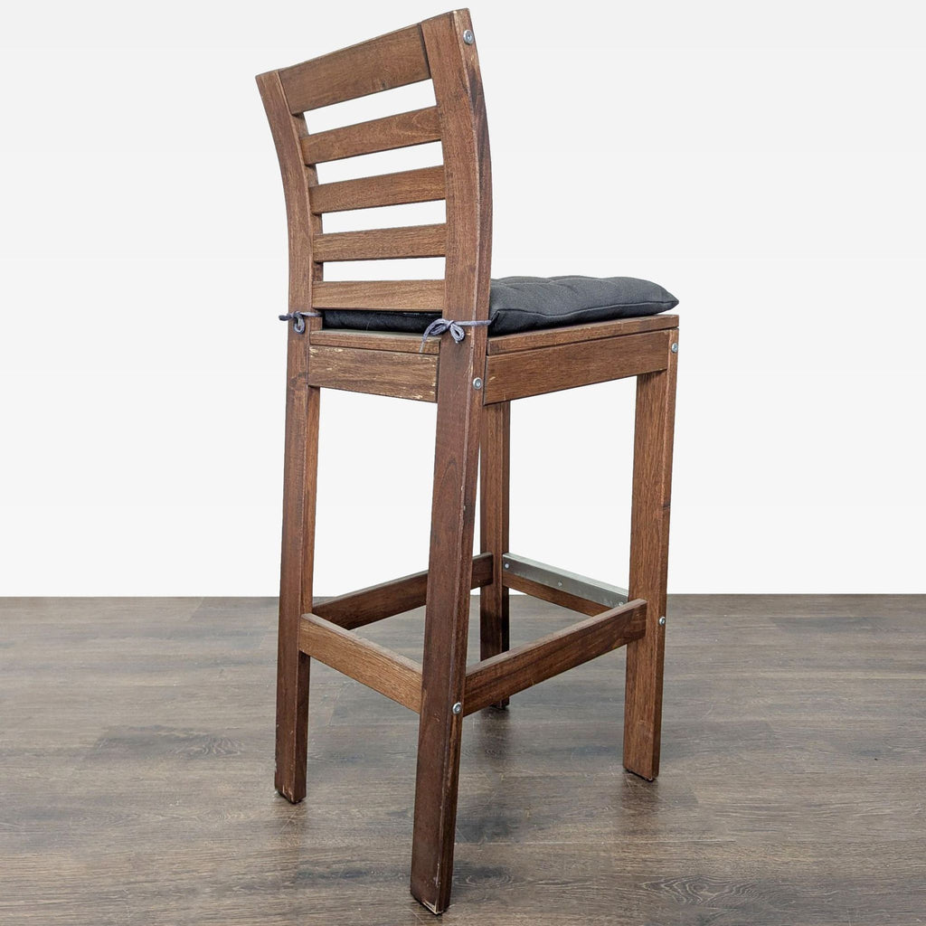 2. Angled view of a tall wooden stool with ladder-back design and a padded black cushion tied to the seat.