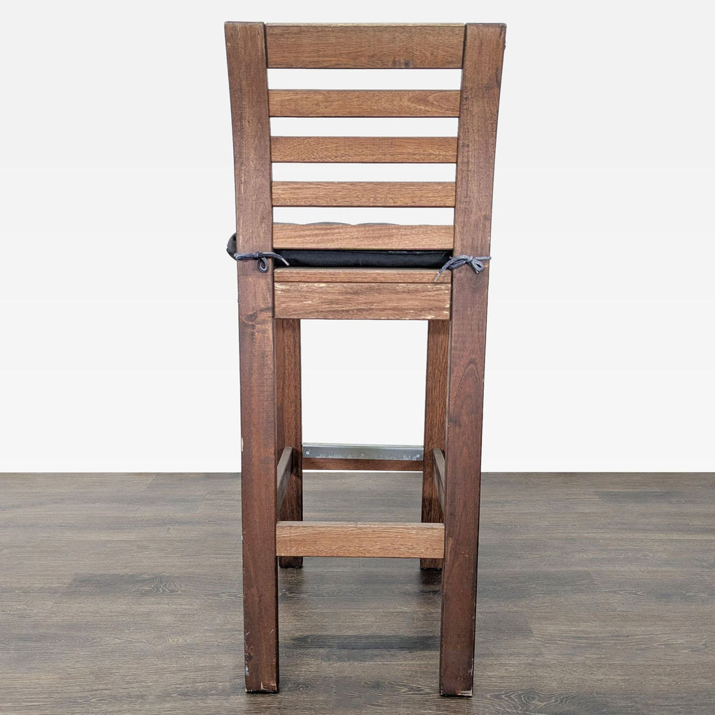 1. Wooden bar stool with slatted backrest and black seat cushion, shown from the back on a wooden floor.