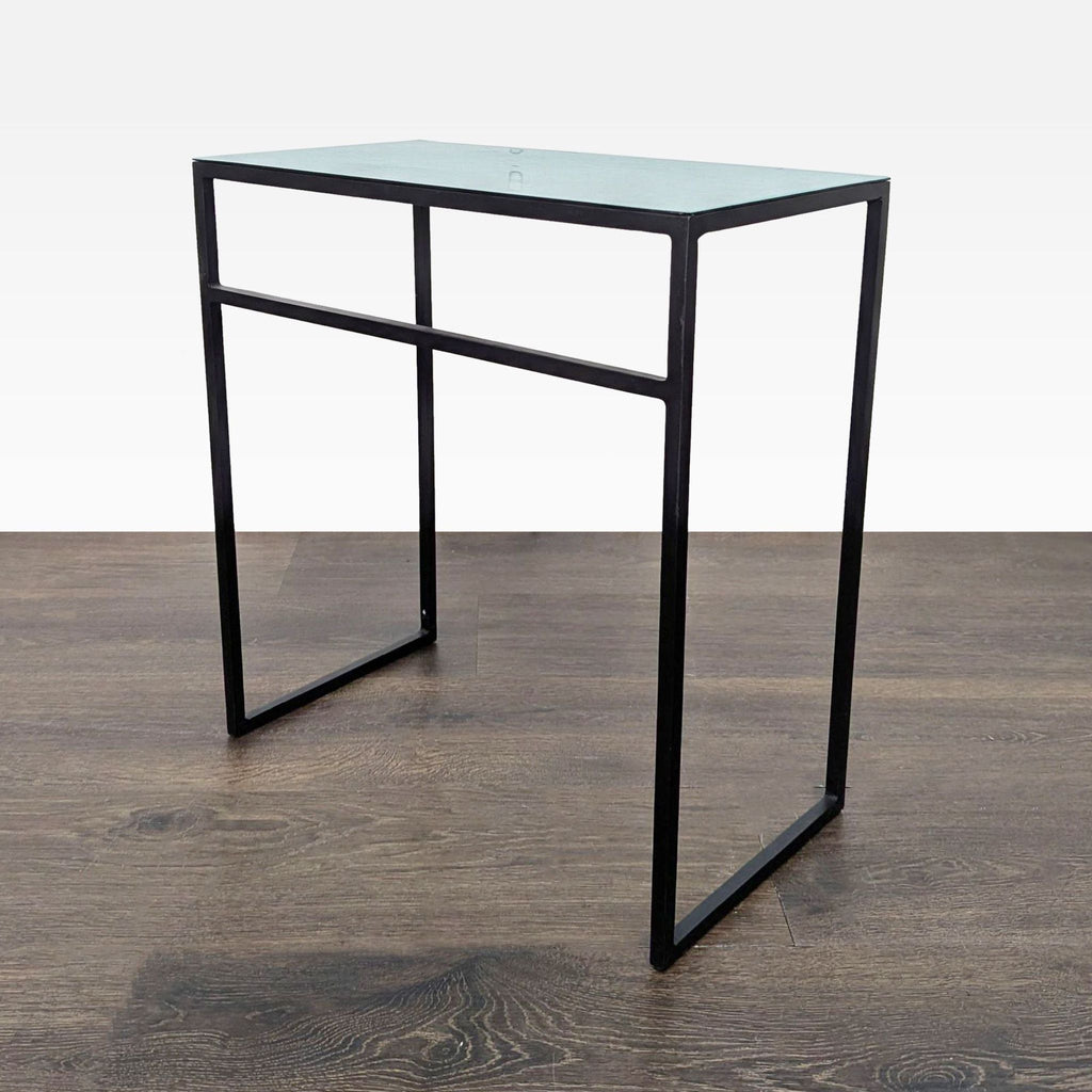 2. Single CB2 side table with a minimalist black metal frame and a rectangular glass top on wooden flooring.